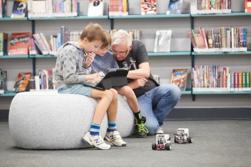 Image of a father and his two sons programming two lego robots with tablets.