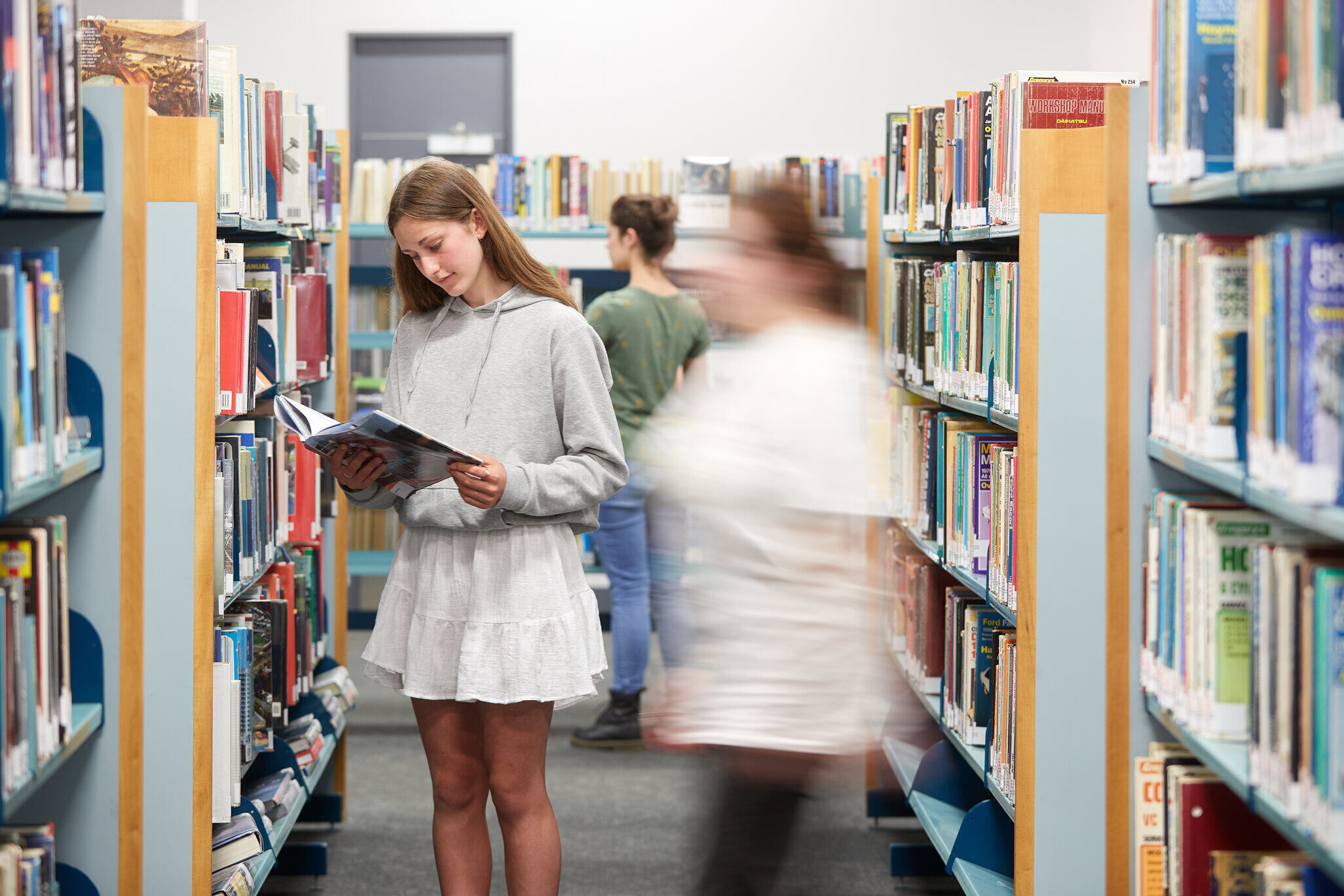 Teenage girl reads a book in the library shelves 