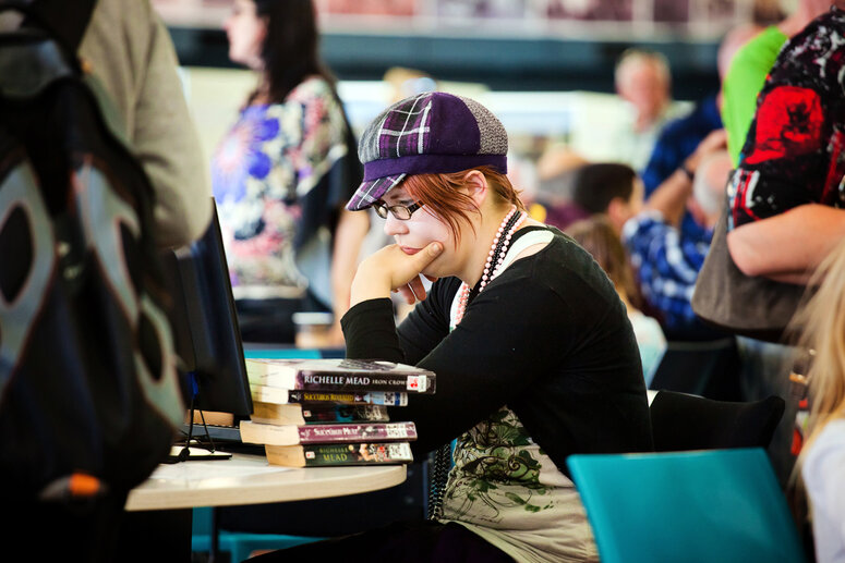 Woman with a pile of books looks intently at a screen